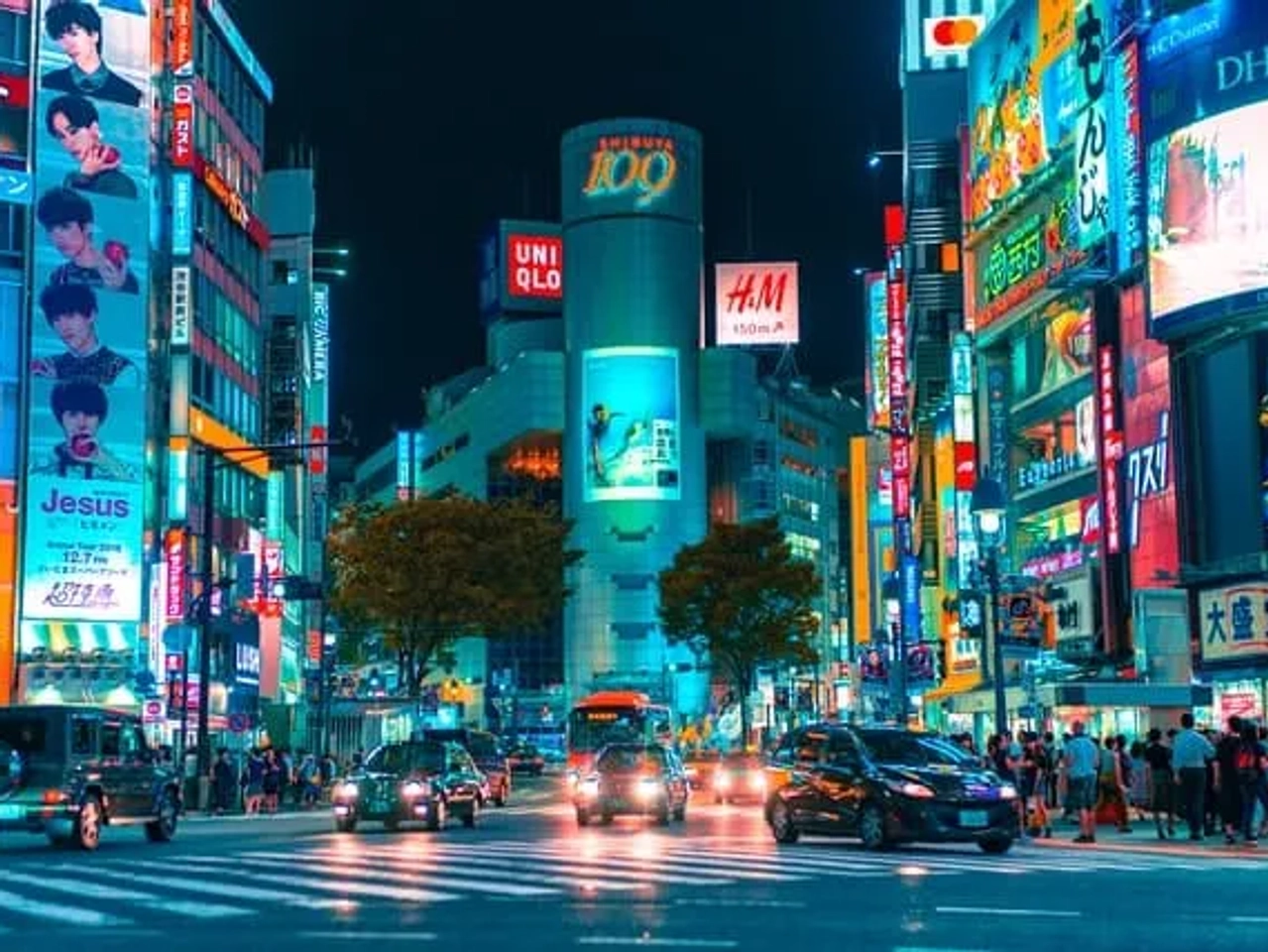 vista de uma avenida durante a noite com carros e pessoas em Shibuya no Japão