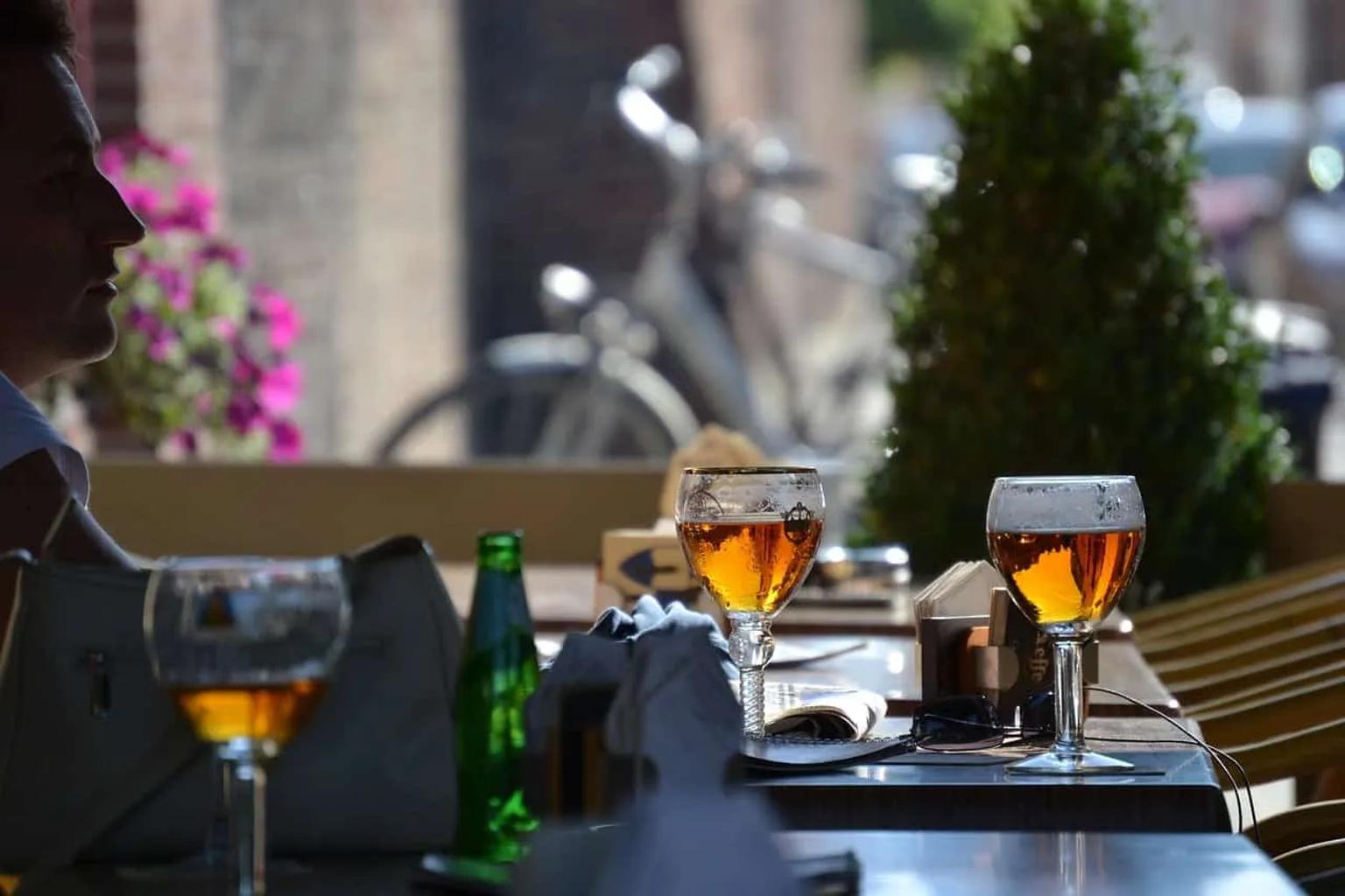Dos copas de cerveza y una botella en una mesa al aire libre.