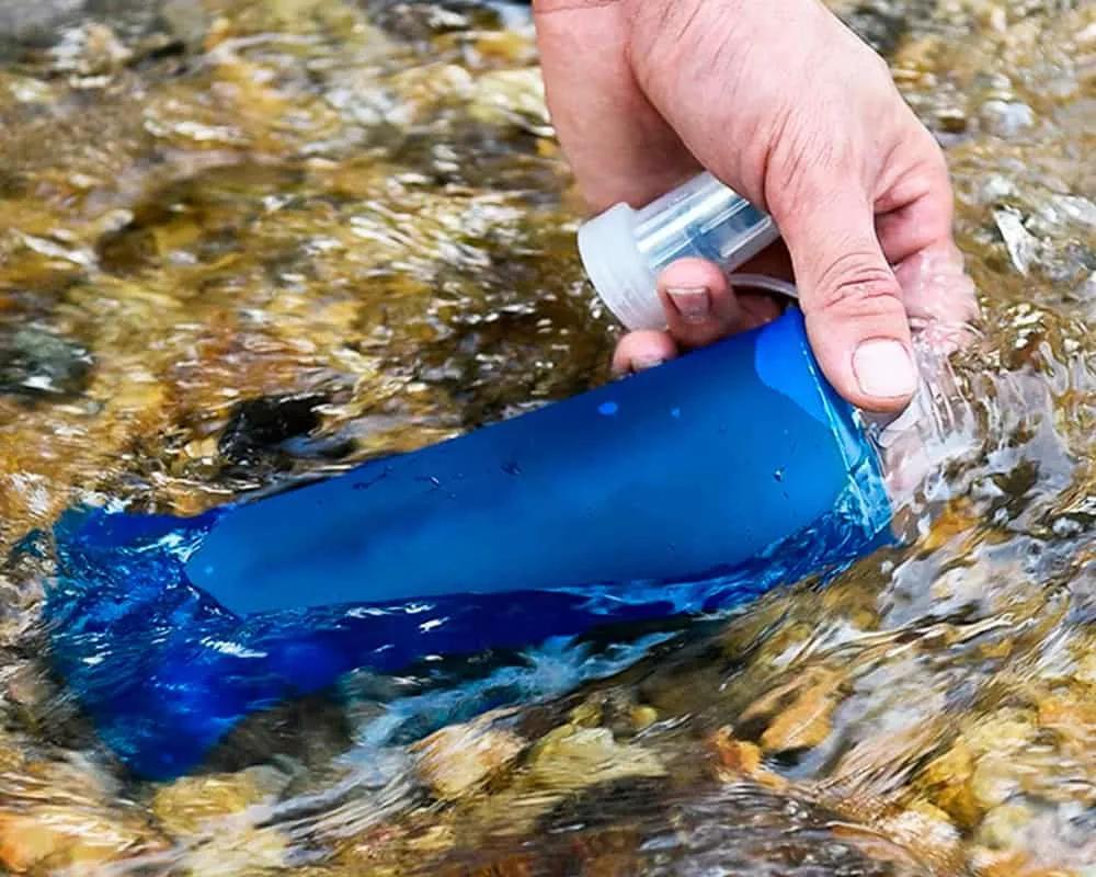 Persona llenando una botella azul con agua de un río.