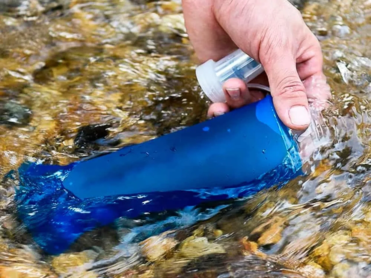 Persona llenando una botella azul con agua de un río.