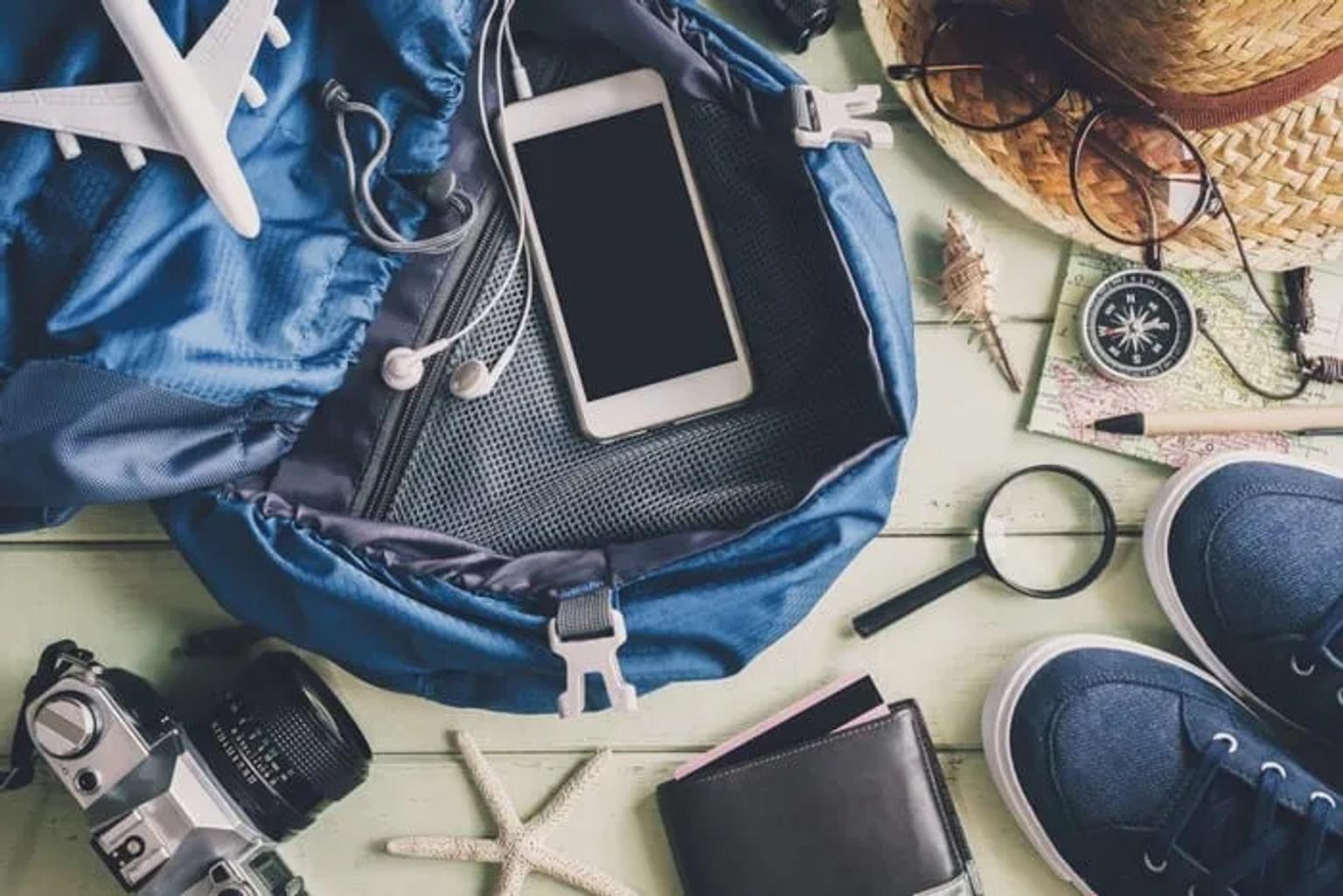 Mochila abierta con accesorios de viaje: teléfono, cámara, mapa y calzado.