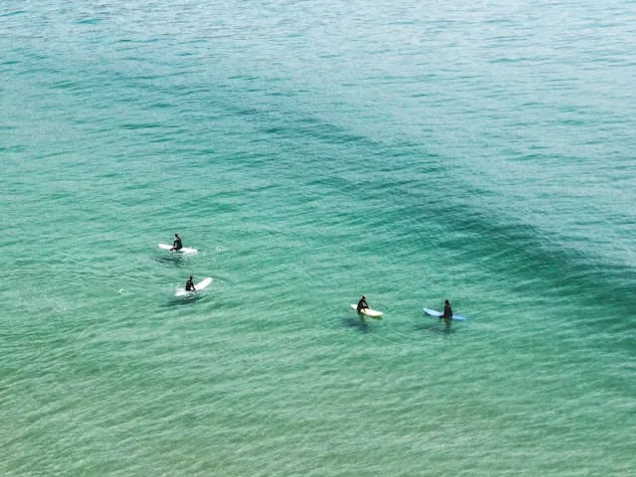 4 pessoas a surfar em mar azul turquesa