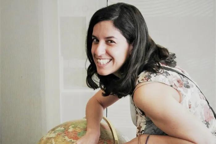 Mujer sonriente junto a un globo terráqueo, en un ambiente luminoso.