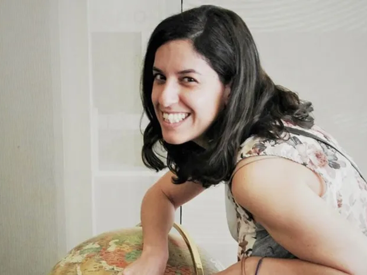 Mujer sonriente junto a un globo terráqueo, en un ambiente luminoso.