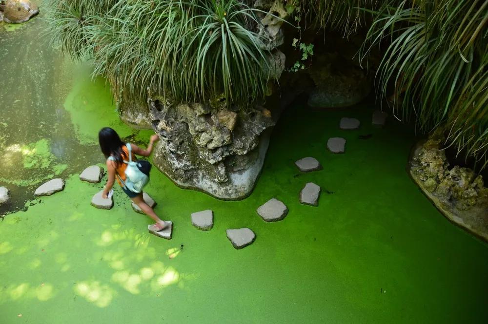 mulher jovem atravessa o lago da quinta pisando as pedras brancas