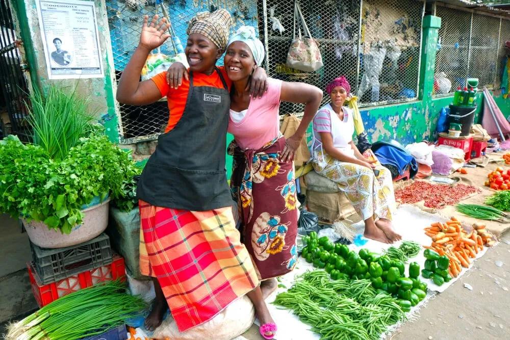 mulheres sorriem num mercado de vegetais em maputo