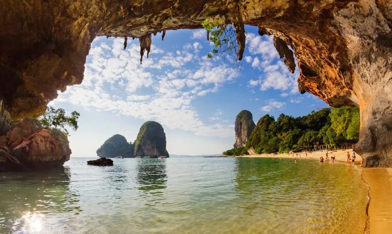 Spiaggia di Krabi in Thailandia vista da una grotta, con mare cristallino, sabbia dorata e alte formazioni rocciose sullo sfondo.
