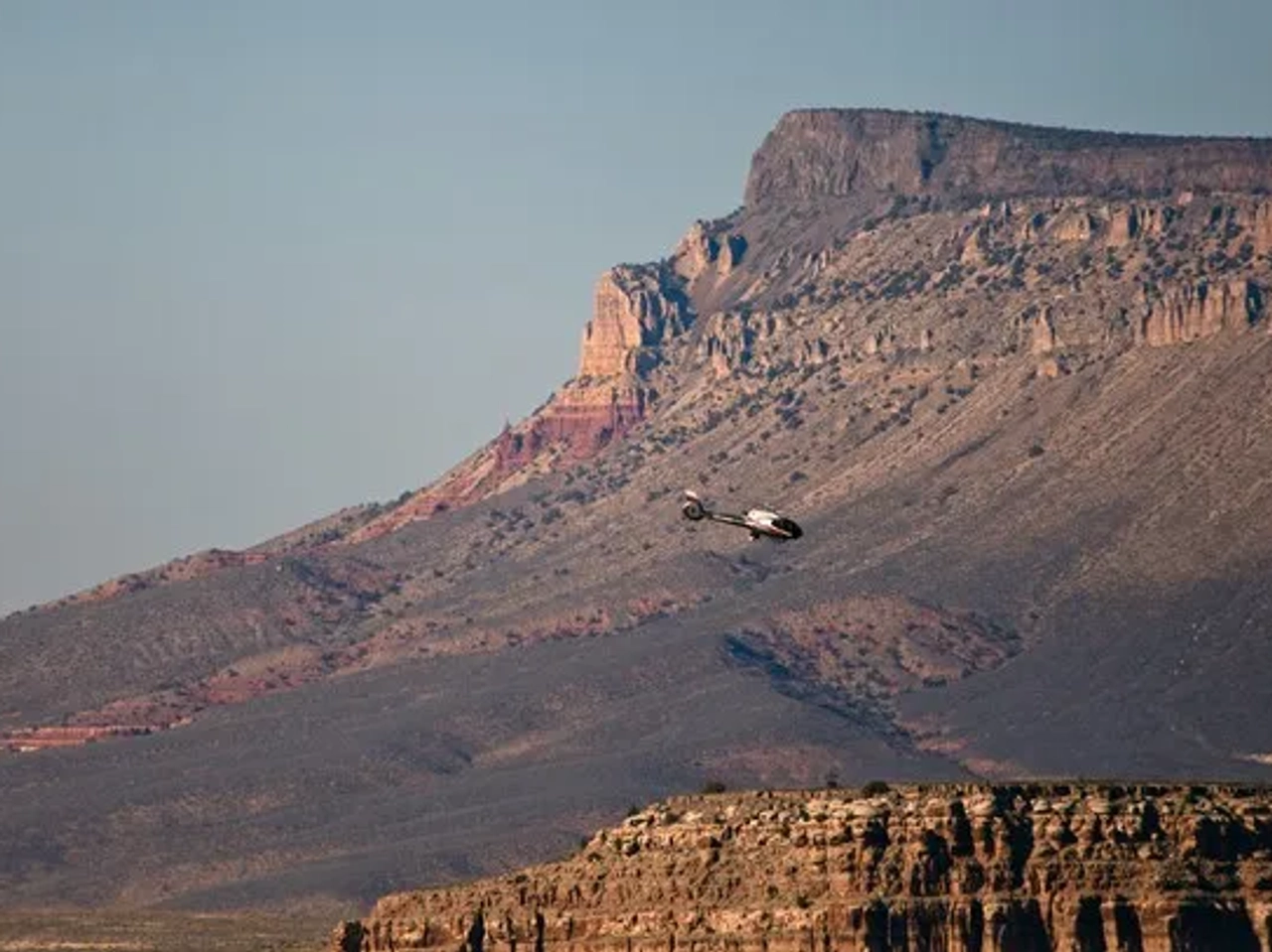 Helicóptero sobrevolando el Gran Cañón, con montañas de fondo.