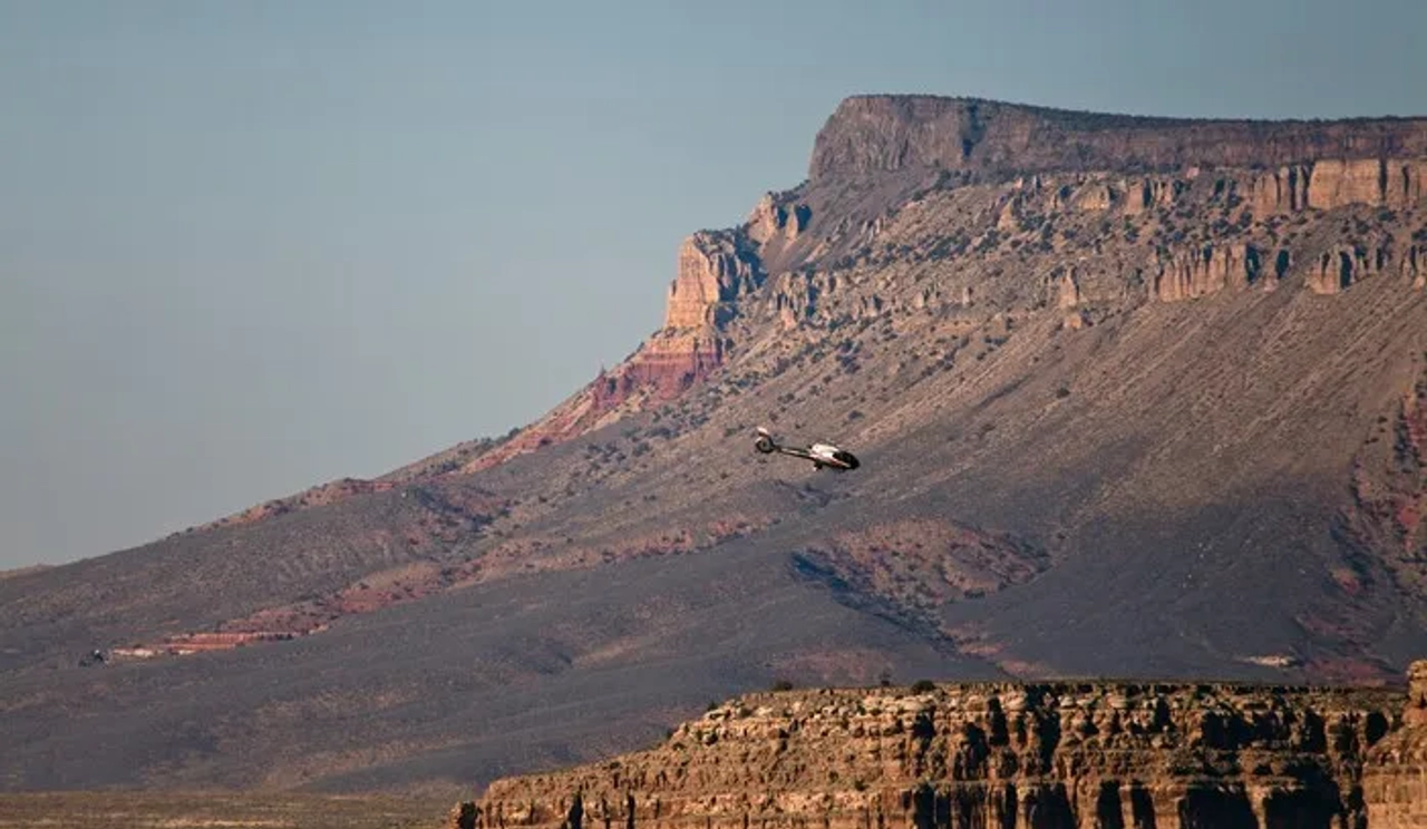 Helicóptero sobrevolando el Gran Cañón, con montañas de fondo.