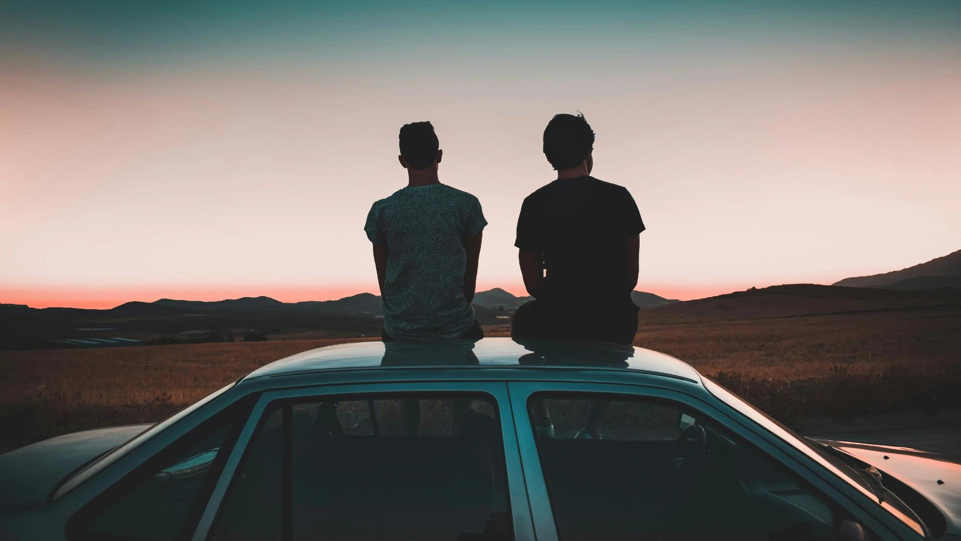 Dos amigos contemplan la puesta de sol sobre un coche financiado tras haber contratado un seguro de vida para proteger la inversión 
