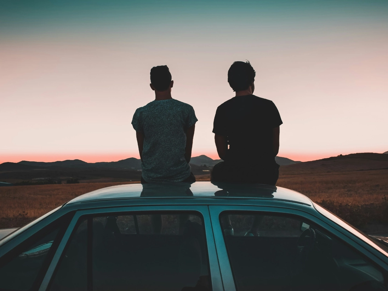 Dos amigos contemplan la puesta de sol sobre un coche financiado tras haber contratado un seguro de vida para proteger la inversión
