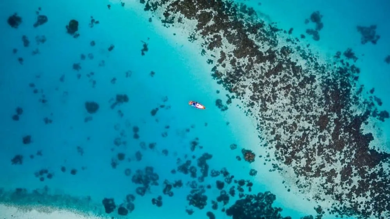 Vista aérea de un bote en aguas turquesas rodeado de arrecifes en Maldivas.