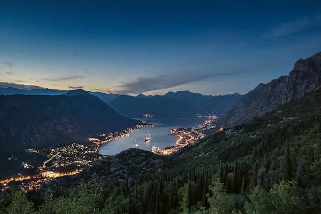 vista de kotor em montenegro ao por do sol, com luzes das casas e barcos a andar no mar
