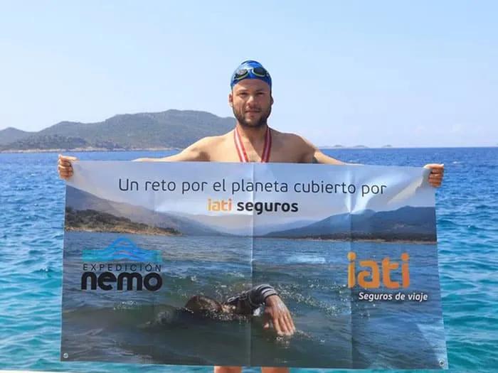 Hombre en la playa sostiene un cartel sobre el compromiso de IATI Seguros con el planeta.