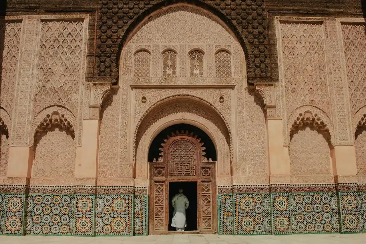 Ingresso decorato della Madrasa Ben Youssef a Marrakech, con archi scolpiti, mosaici marocchini e dettagli tradizionali da visitare durante un itinerario di 7 giorni in Marocco.