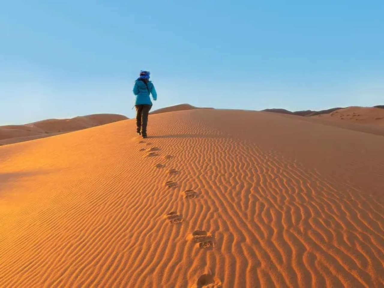 Pessoa caminhando sobre dunas de areia no deserto ao amanhecer.