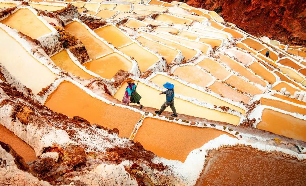 Personas caminando entre las salineras de Maras, Perú, con aguas salinas de colores.