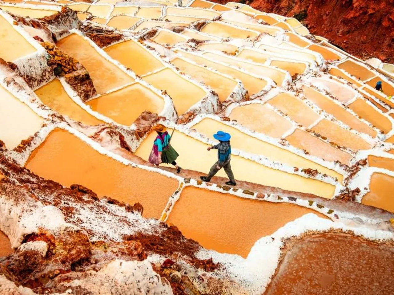 Personas caminando entre las salineras de Maras, Perú, con aguas salinas de colores.