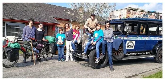 Familia y amigos posando junto a un vehículo antiguo y bicicletas.