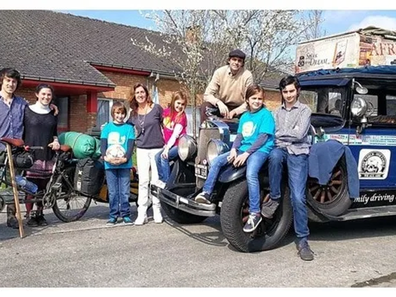 Familia y amigos posando junto a un vehículo antiguo y bicicletas.