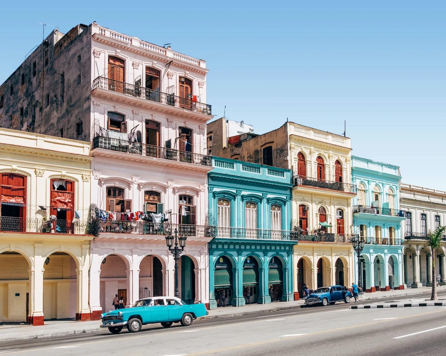 Colorful colonial buildings line a street in Havana, Cuba, with vintage cars parked nearby.