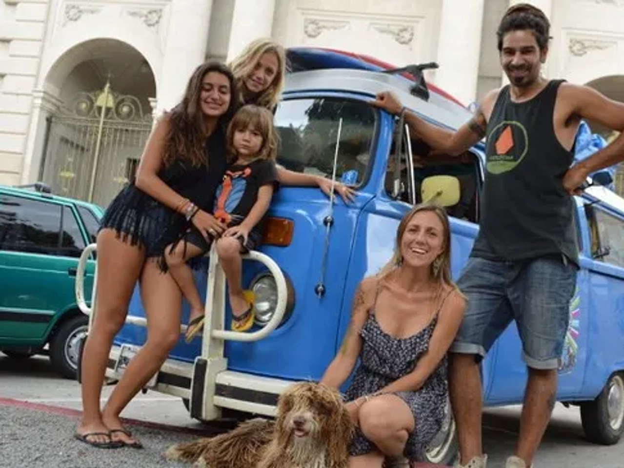 Familia sonriente posando frente a una furgoneta azul con un perro.