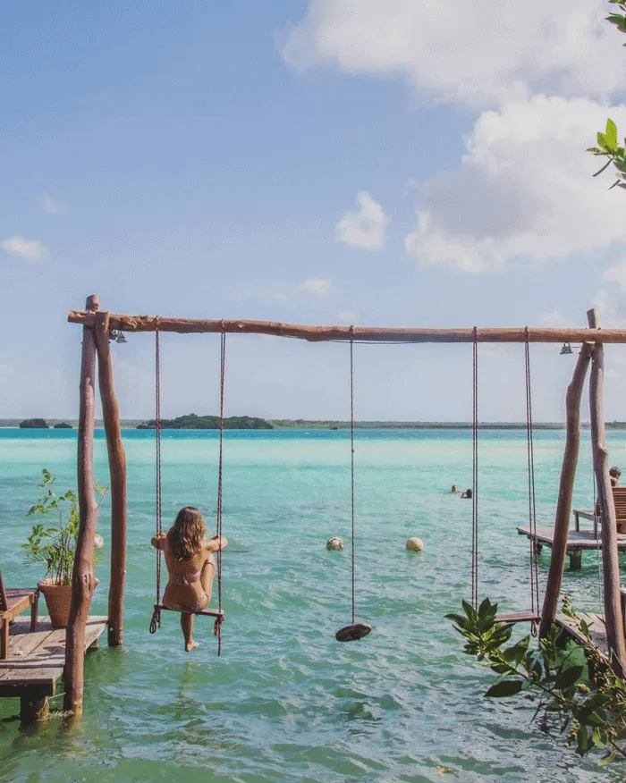 Mujer en un columpio sobre agua turquesa, rodeada de naturaleza y tranquilidad.