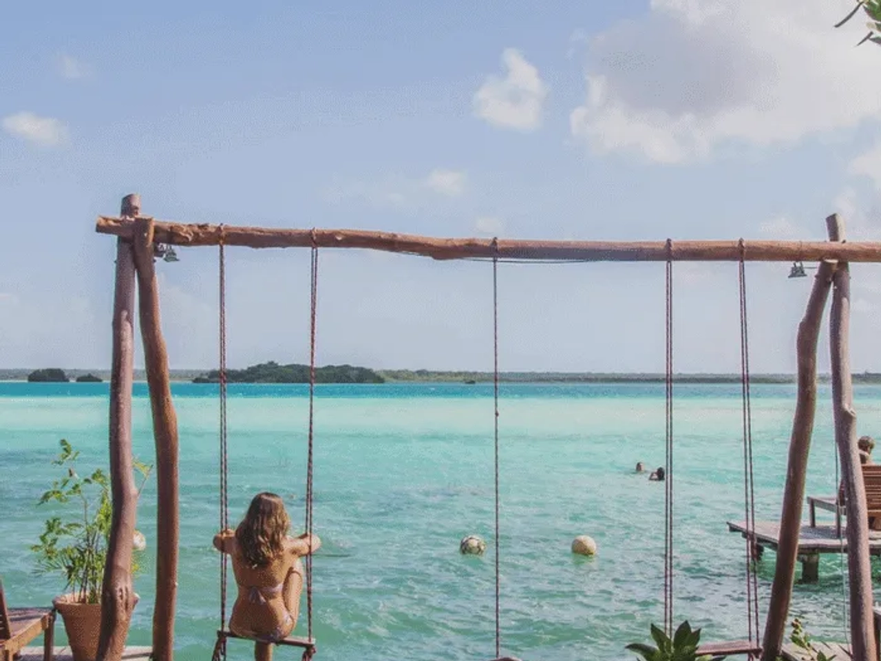Mujer en un columpio sobre agua turquesa, rodeada de naturaleza y tranquilidad.