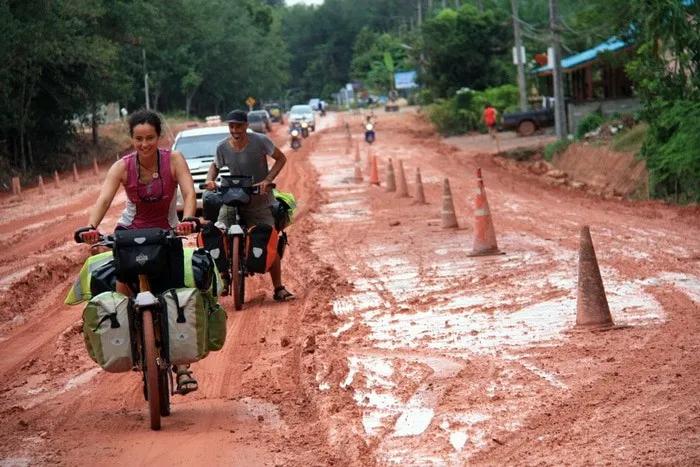Ciclistas recorriendo un camino de tierra con vehículos y conos de señalización.