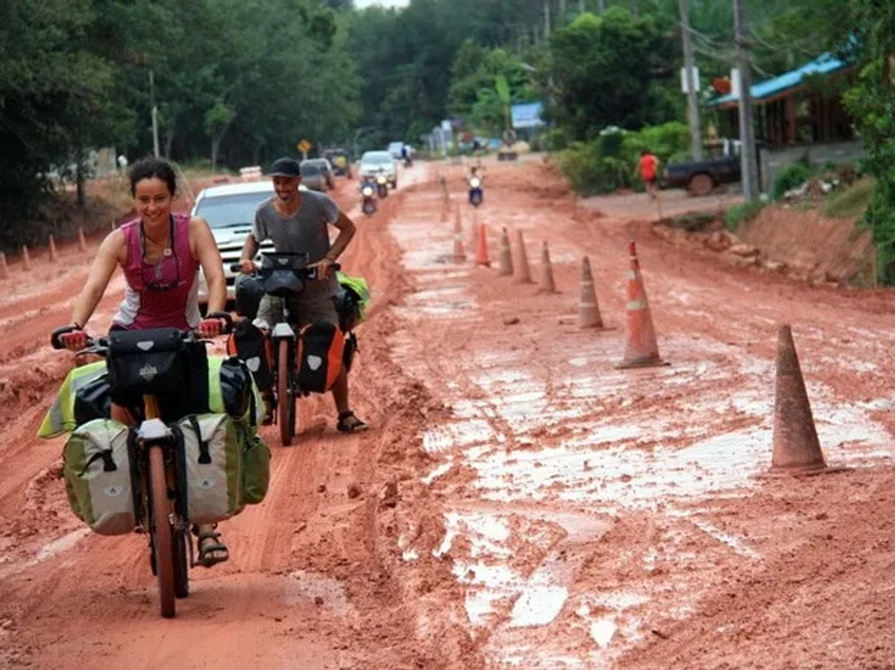 Ciclistas recorriendo un camino de tierra con vehículos y conos de señalización.