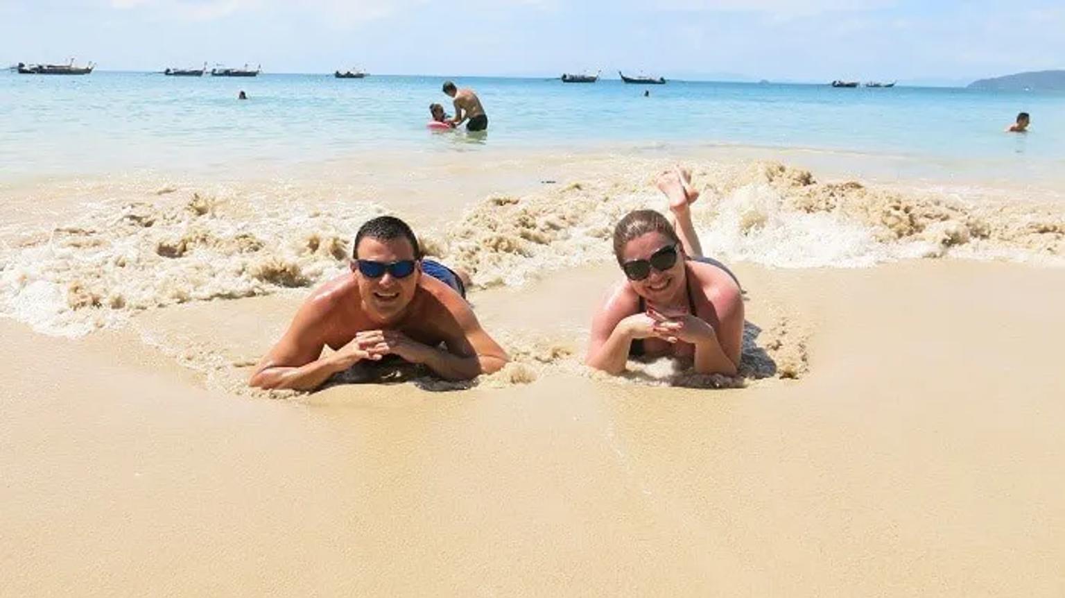 Pareja disfrutando en la playa, recostados sobre la arena y el agua.