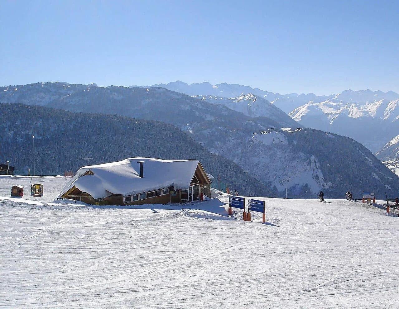 Estância de esqui com montanhas cobertas de neve e um chalé ao fundo.