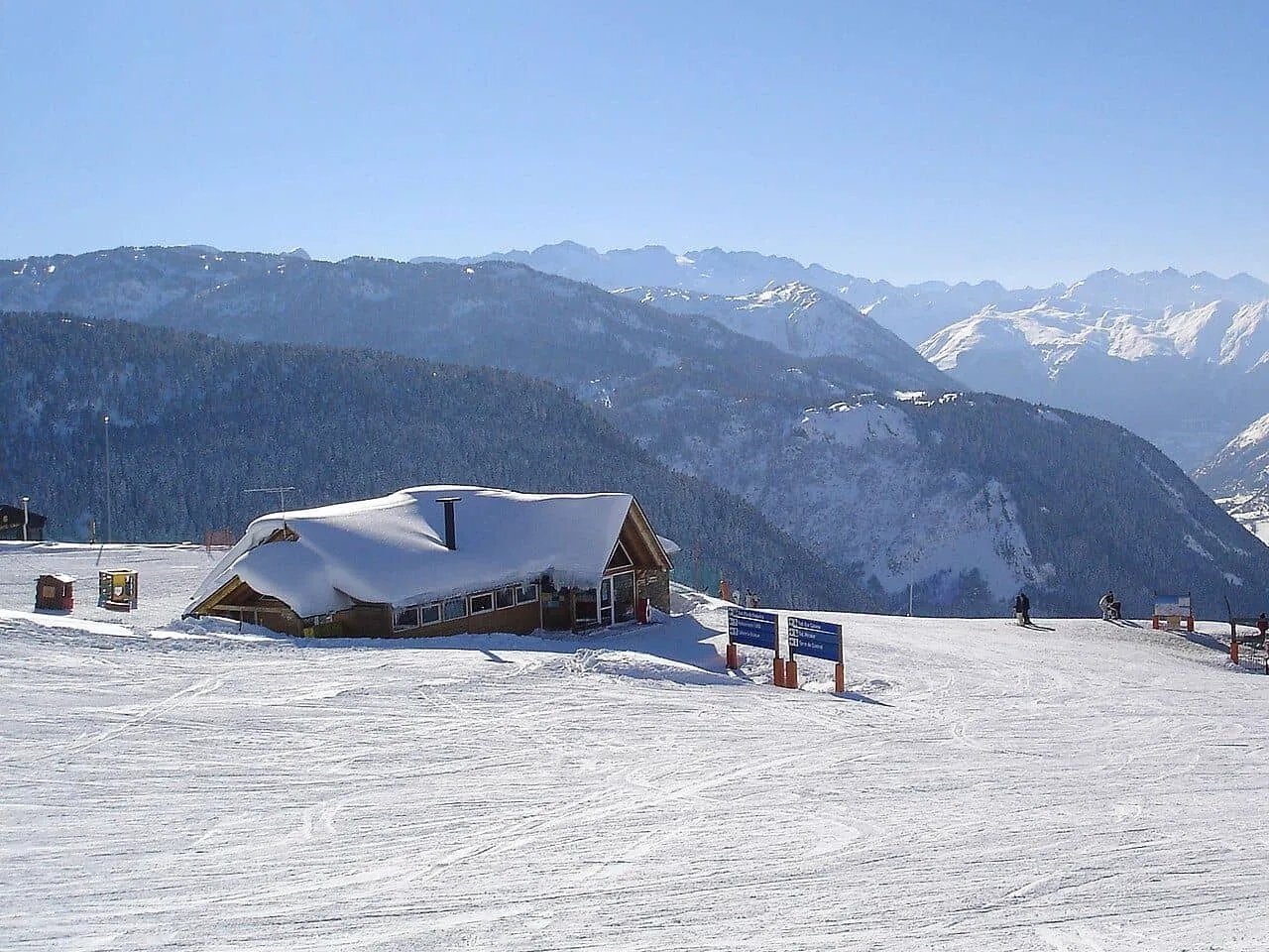Estância de esqui com montanhas cobertas de neve e um chalé ao fundo.