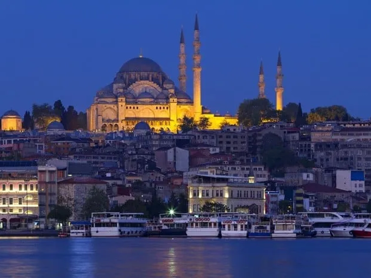 Vista noturna da Mesquita Suleymaniye em Istambul, com barcos no rio.