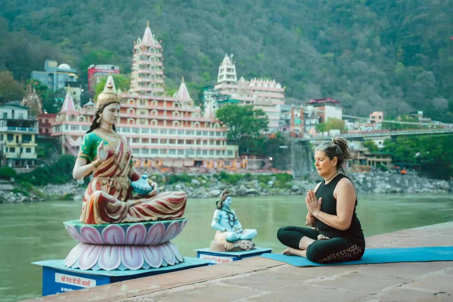 Mulher meditando em frente a estátuas em um ambiente tranquilo à beira do rio.