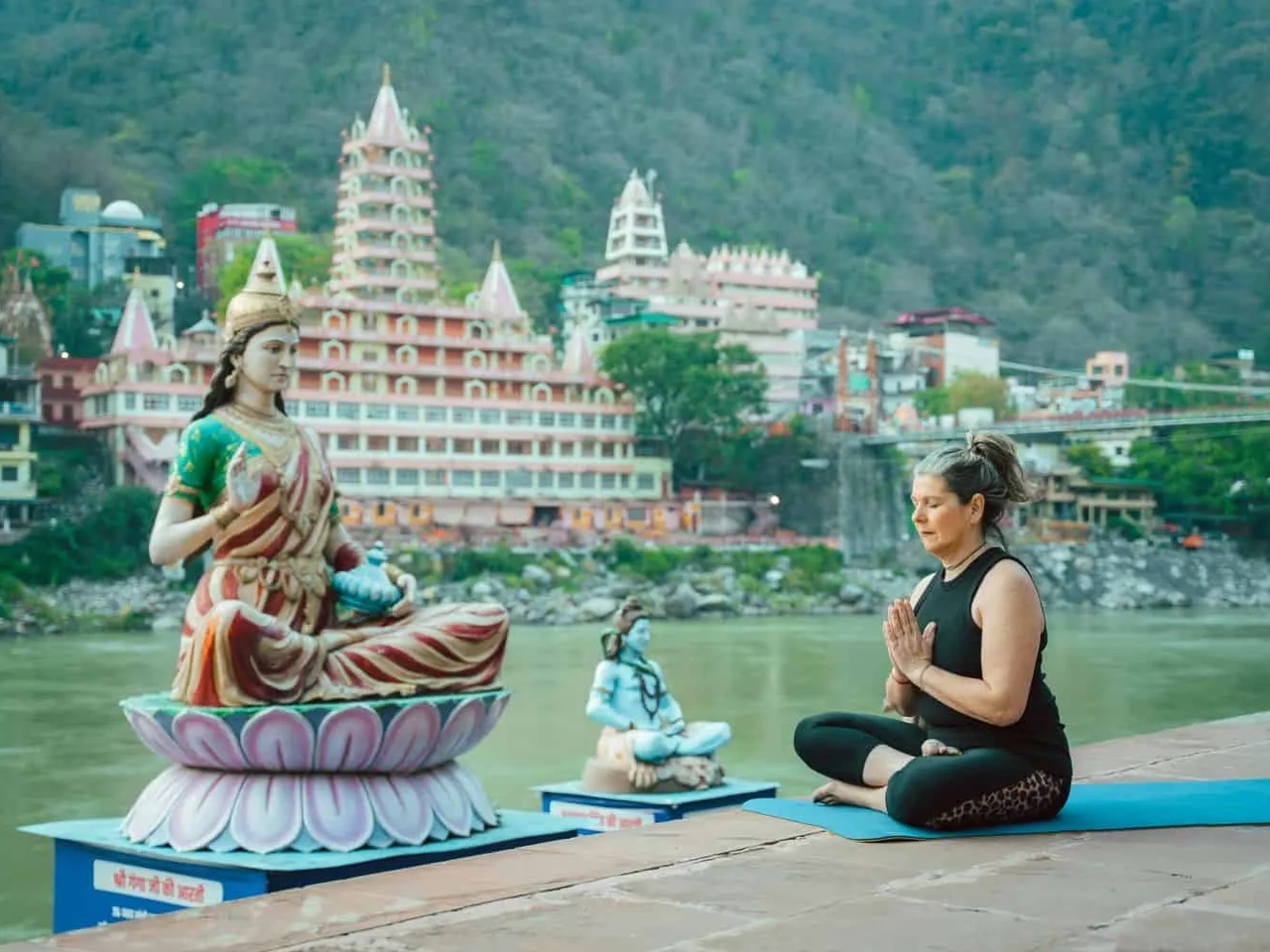 Mulher meditando em frente a estátuas em um ambiente tranquilo à beira do rio.