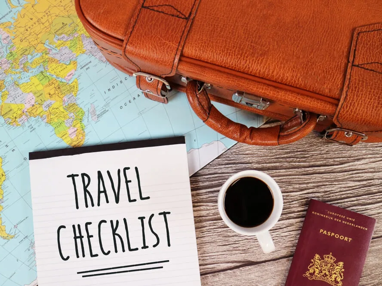 checklist, cafe e mala pousados em cima de um mapa mundo