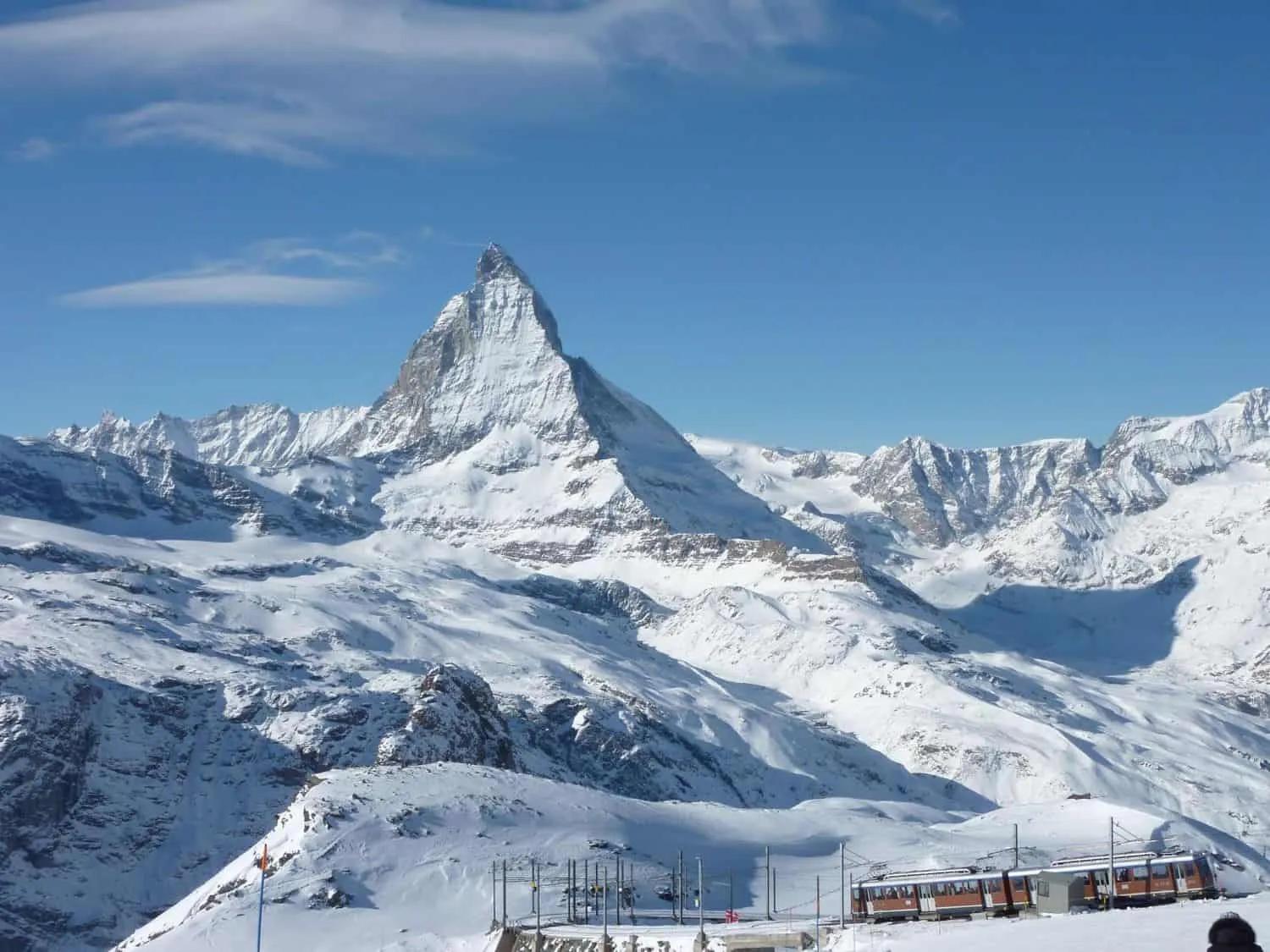 Montanha coberta de neve com o pico do Matterhorn ao fundo. Céu azul claro.