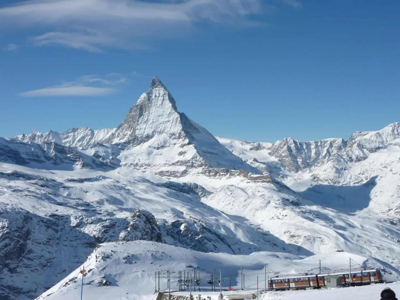 Montanha coberta de neve com o pico do Matterhorn ao fundo. Céu azul claro.