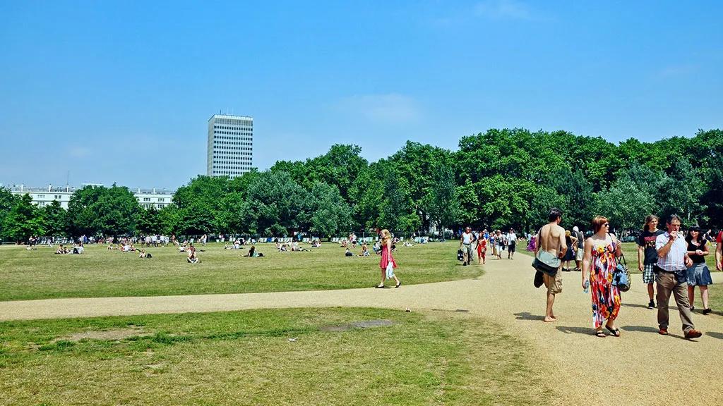 Parque em Londres com pessoas caminhando e relaxando em um dia ensolarado.