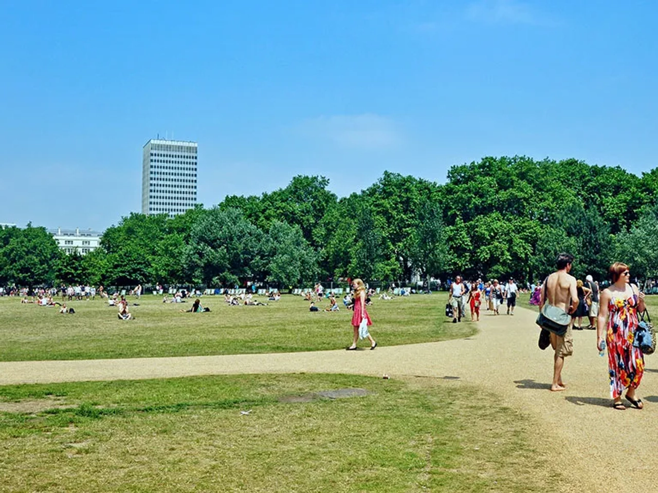 Parque em Londres com pessoas caminhando e relaxando em um dia ensolarado.