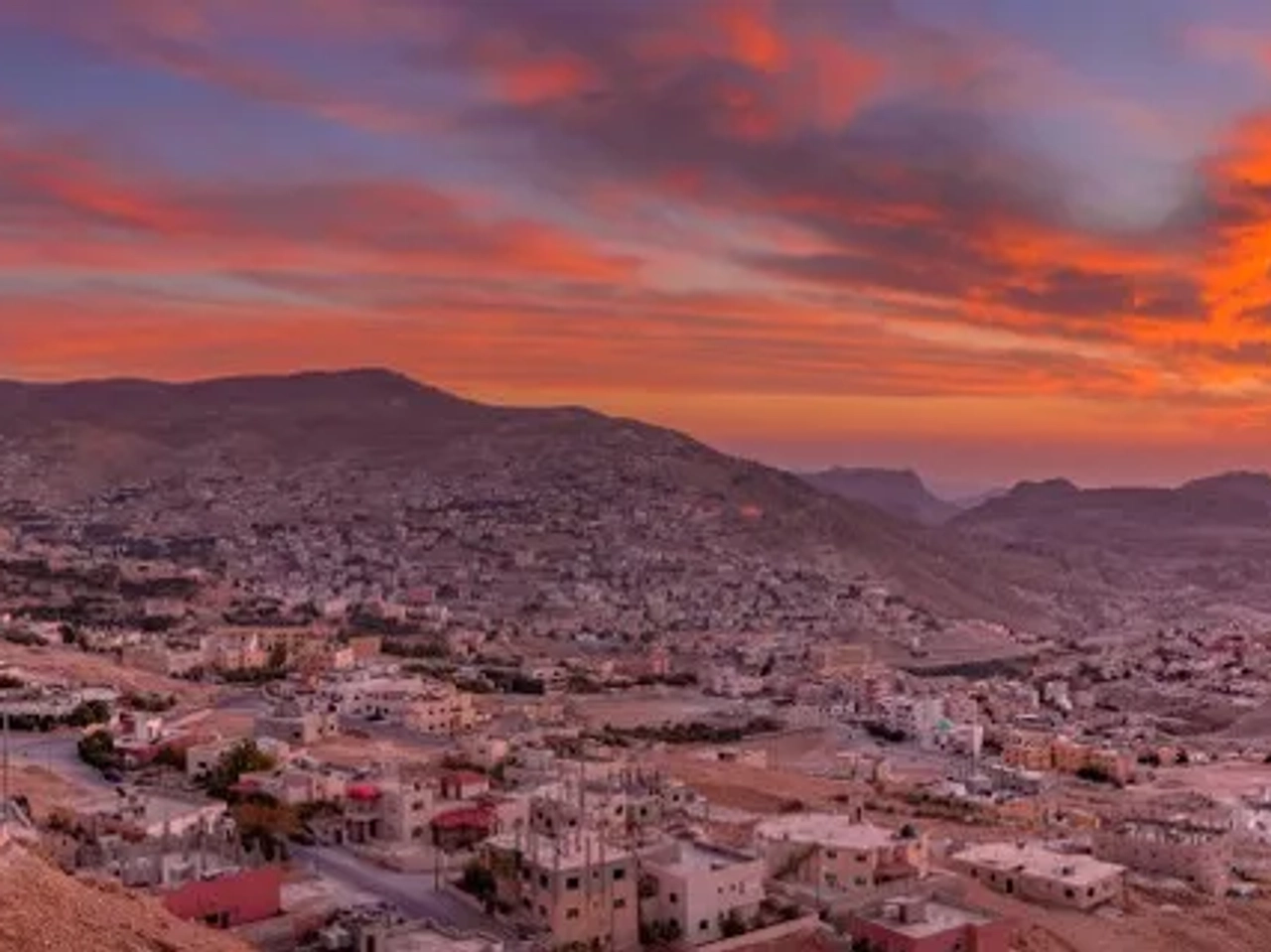 Vista panorâmica de Petra ao pôr do sol, destacando montanhas e construções históricas.