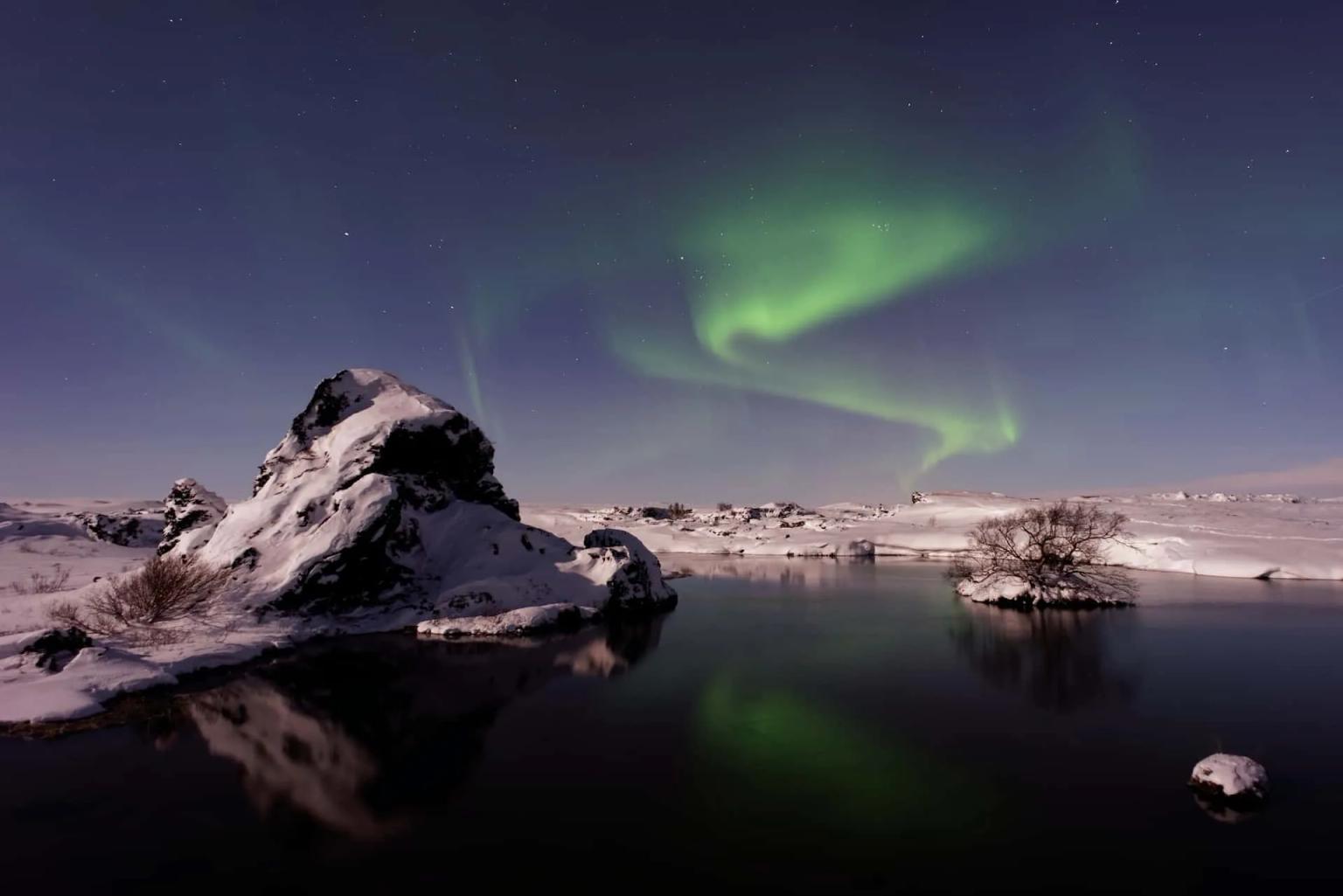 Auroras boreais iluminam o céu noturno sobre uma paisagem nevada na Islândia.