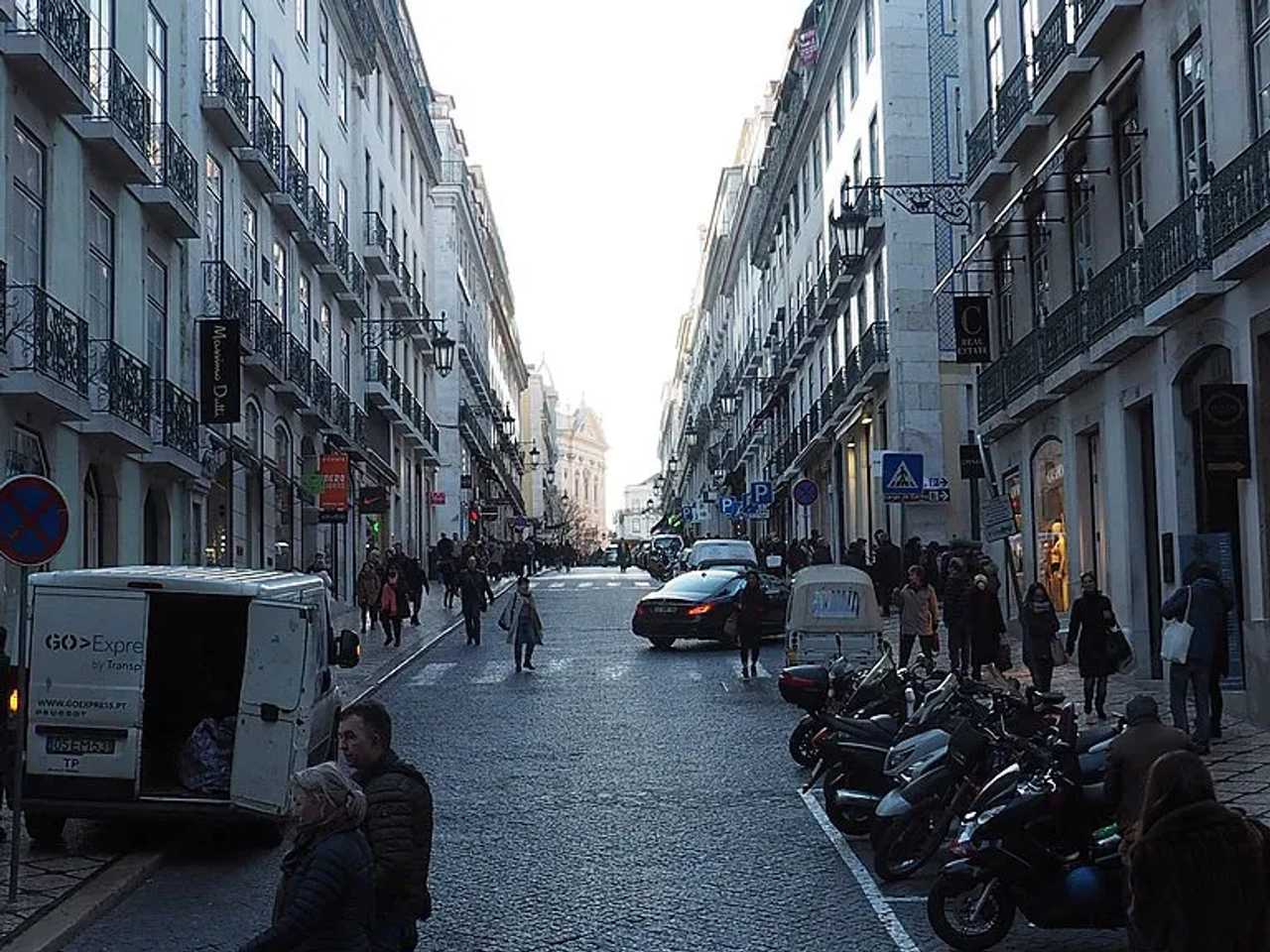 Rua movimentada em Lisboa, com lojas, veículos e pedestres.