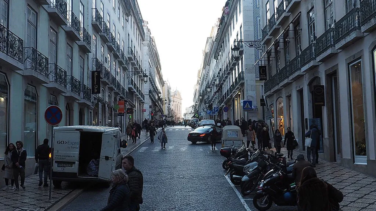 Rua movimentada em Lisboa, com lojas, veículos e pedestres.