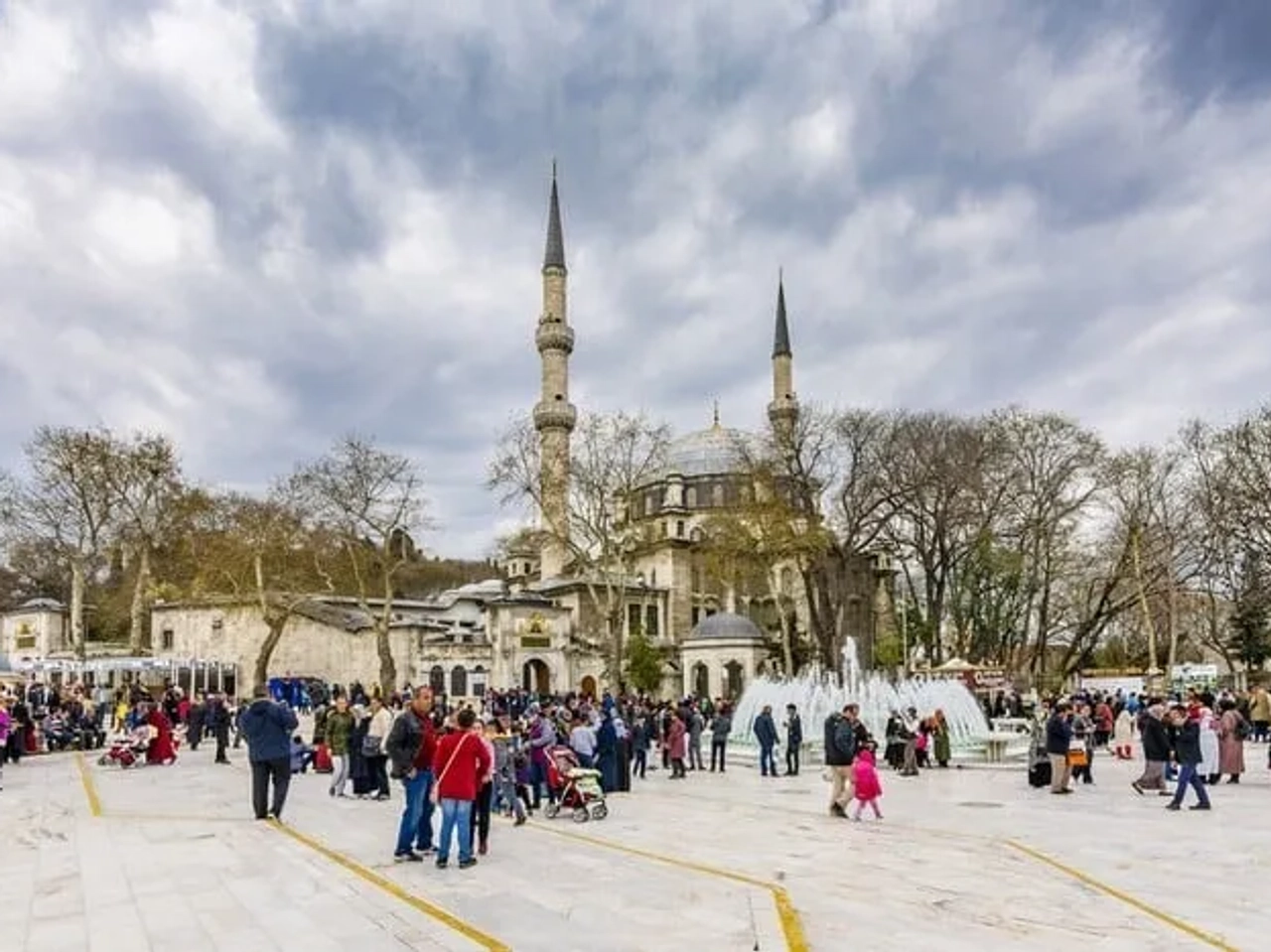 Praça movimentada com a mesquita ao fundo e pessoas ao redor.