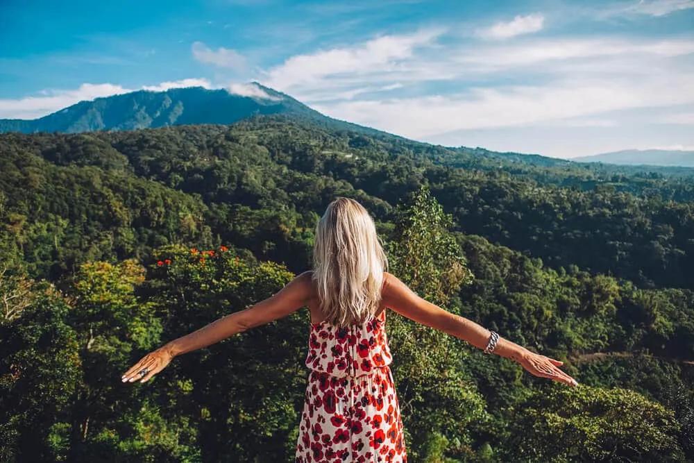 mulher de vestido vermelho e braços abertos contempla a floresta de bali