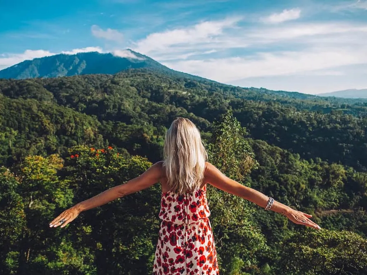 mulher de vestido vermelho e braços abertos contempla a floresta de bali