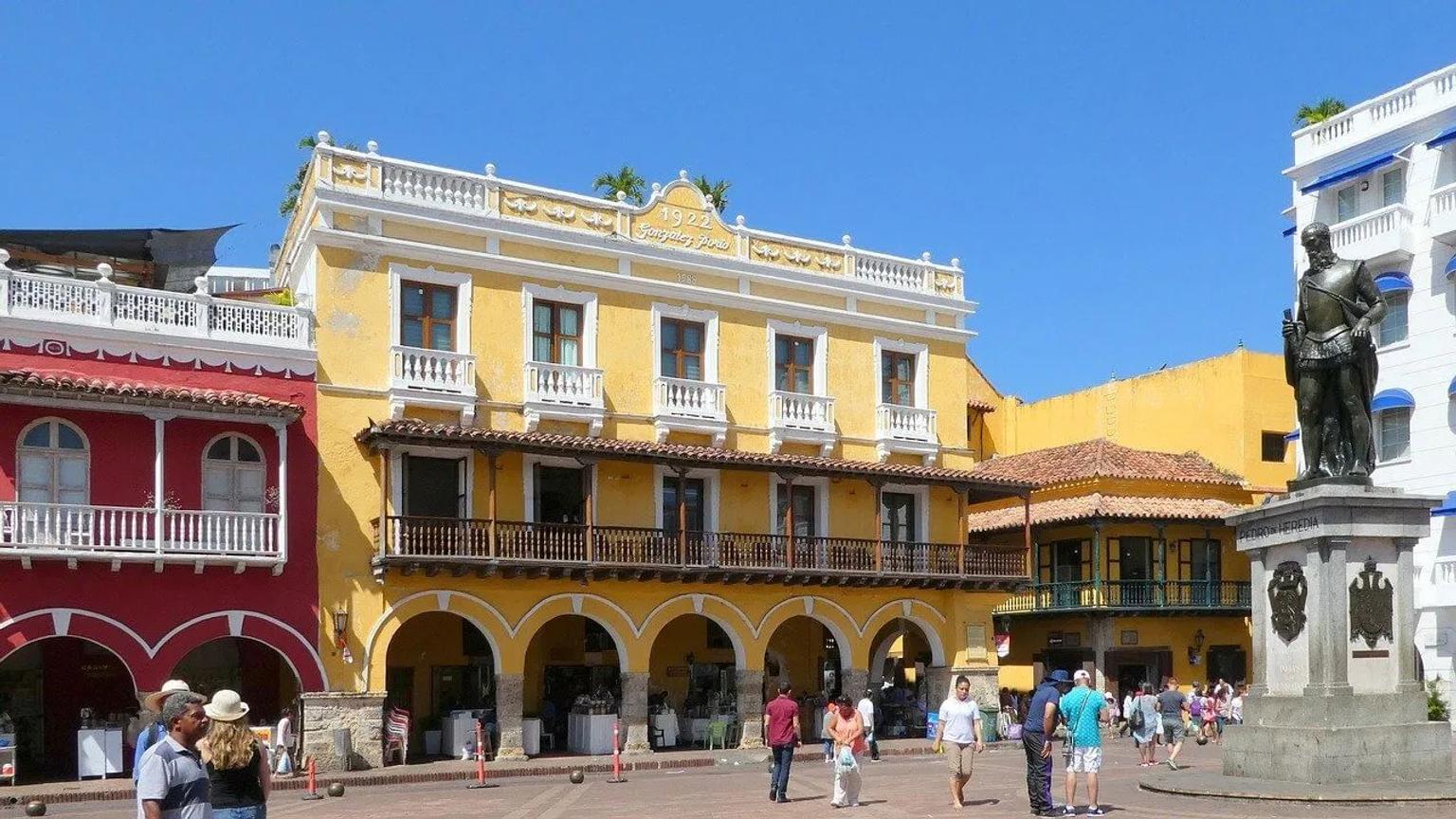 Praça colorida em Cartagena, com edifícios históricos e estátua no centro.