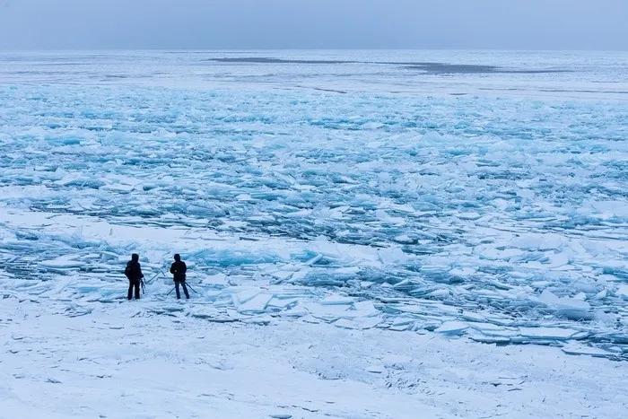 Dos personas observan un lago helado con fragmentos de hielo.